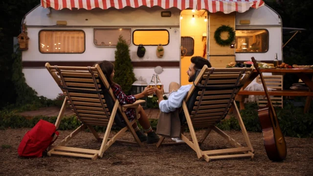 Young couple toasting with bottles of beer near trailer. Camping season