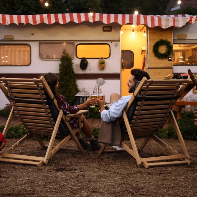 Pareja joven brindando con botellas de cerveza cerca del remolque. Temporada de camping