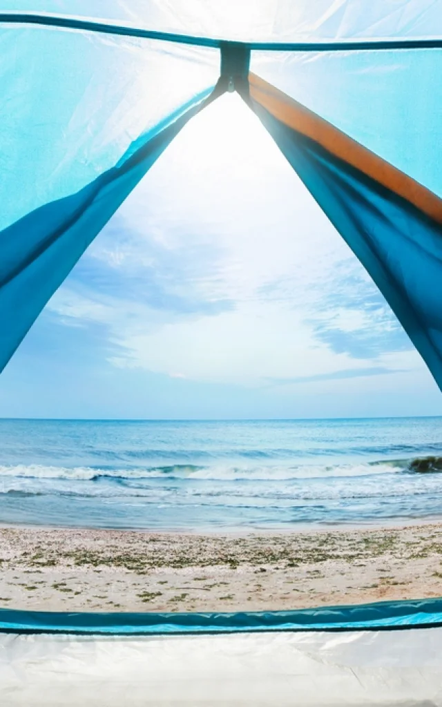 Photo of a sunny day sea shore view from a blue camping tent door.