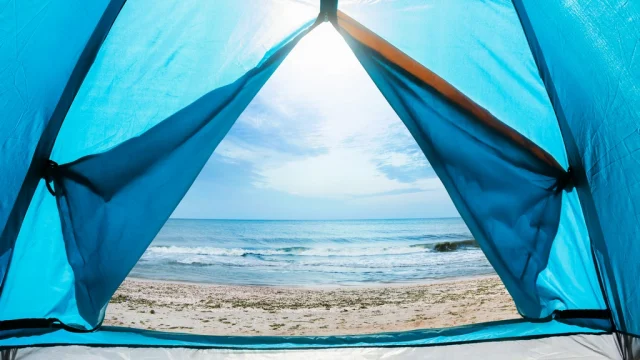 Photo of a sunny day sea shore view from a blue camping tent door.