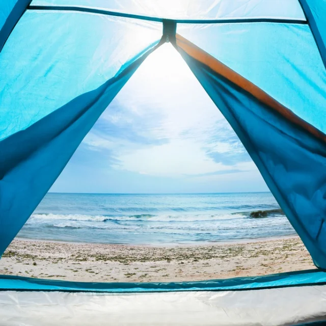 Photo of a sunny day sea shore view from a blue camping tent door.