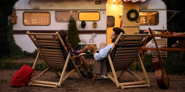 Young couple toasting with bottles of beer near trailer. Camping season