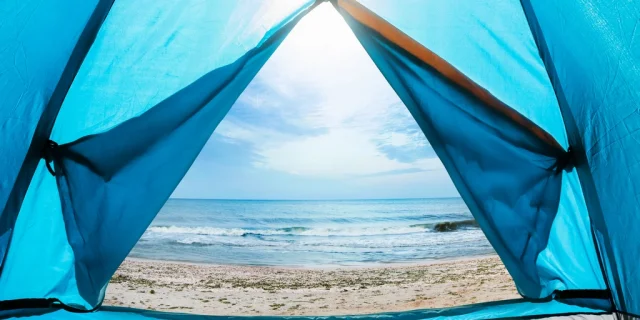 Photo of a sunny day sea shore view from a blue camping tent door.